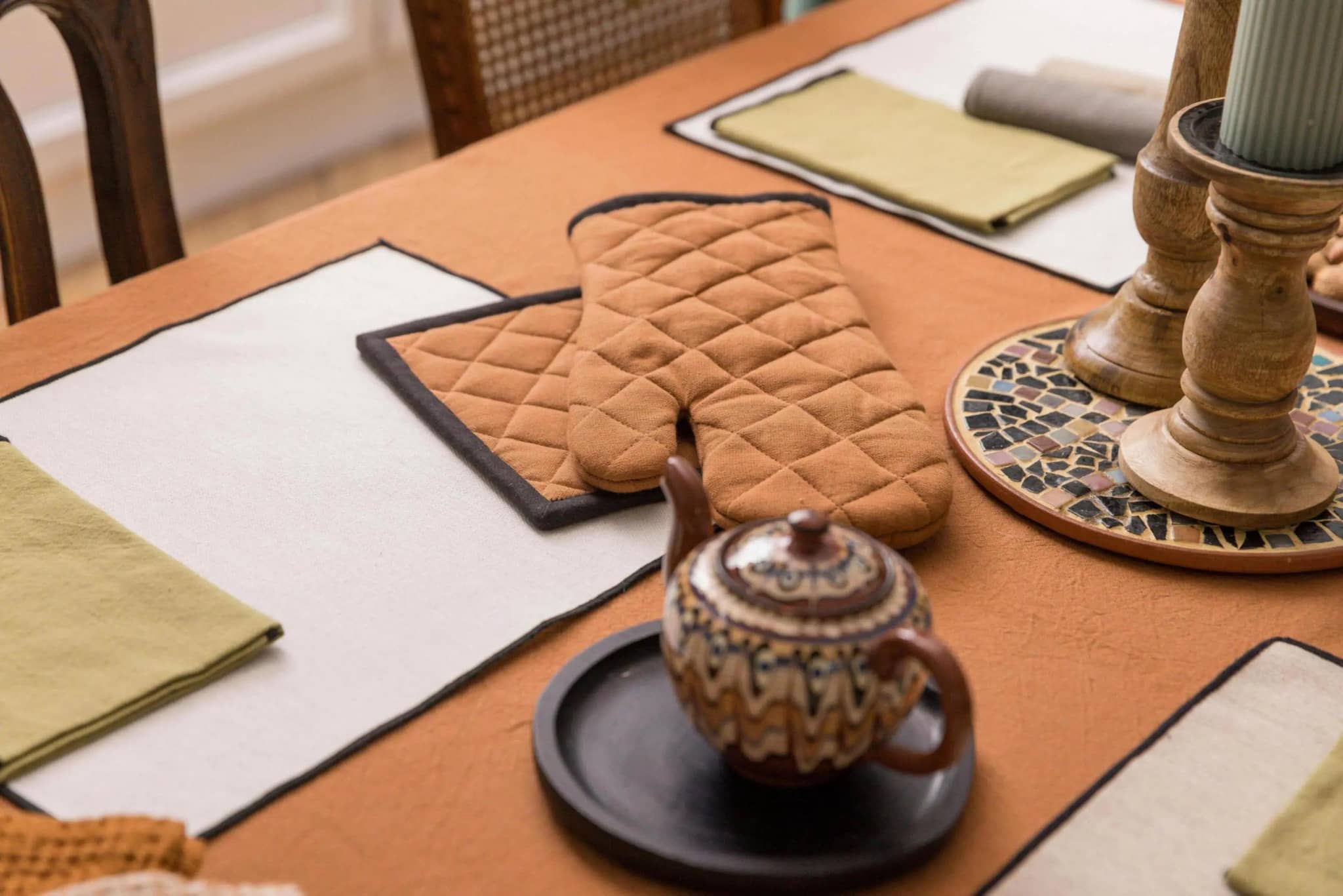 Paire de gant de cuisine en coton marron posé sur une table dressée avec des nappes et serviettes