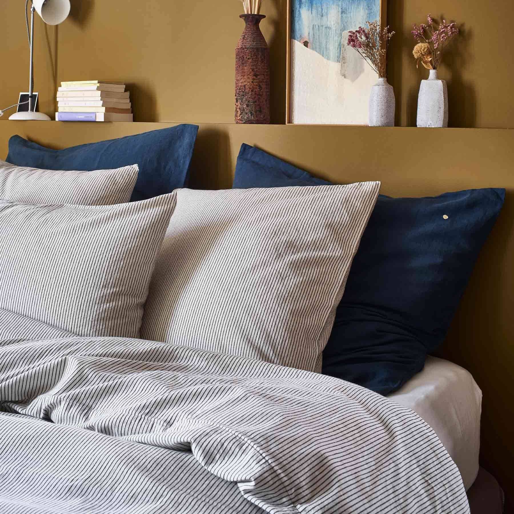 Chambre avec lit décoré de housse de couette coton à rayures beige et coussins bleus