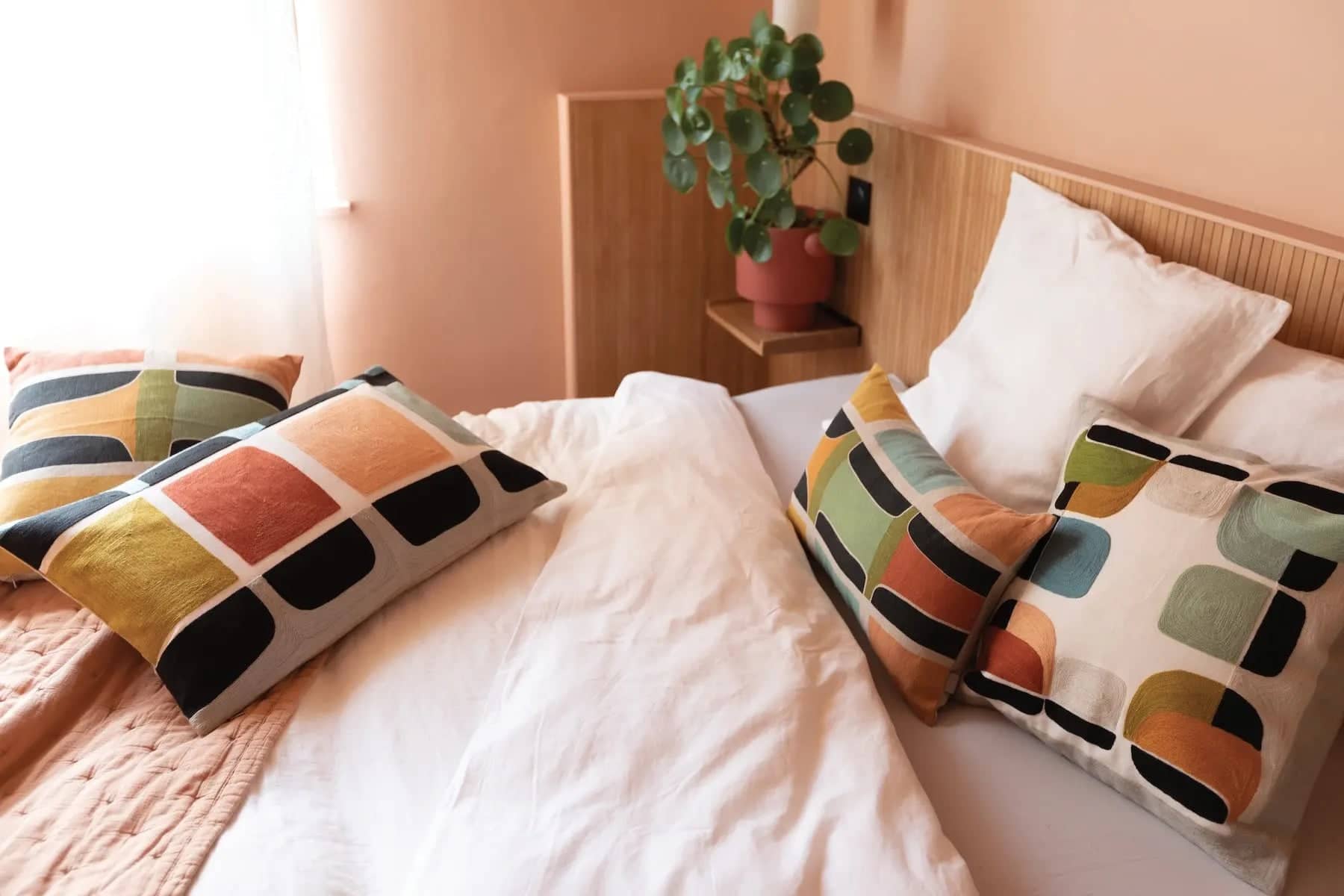 Lit douillet avec des oreillers colorés et un drap en chanvre blanc dans une chambre lumineuse et chaleureuse